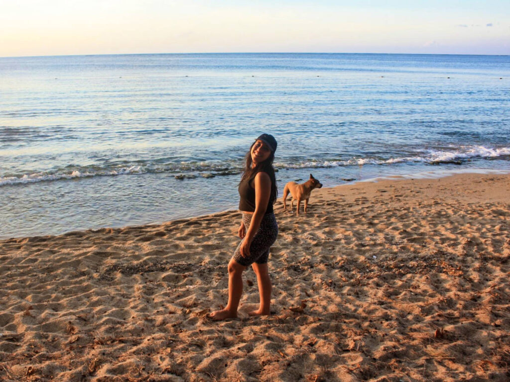 The author Vanessa Ramos, posing for a photo on the beach with a dog, enjoying the sun and waves