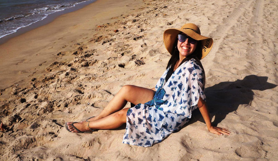 The author smiling to the camera while sitting on the sand by the beach