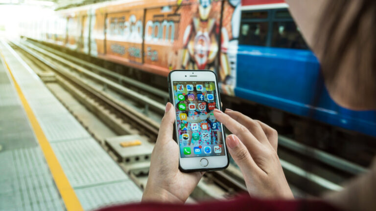 A woman's hands navigating the travel apps on her smartphone at the train station