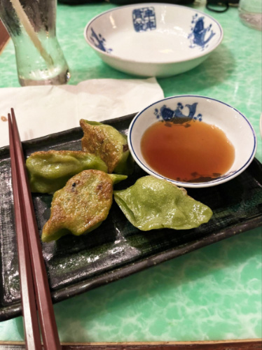 A black squared plate with vegetable potstickers and sauce with chopsticks