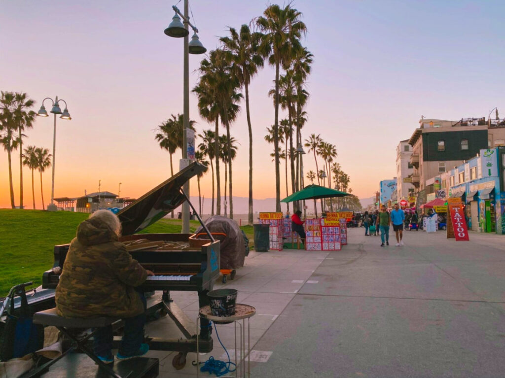 A person playing the piano on Venice Beach boardwalk at sunset