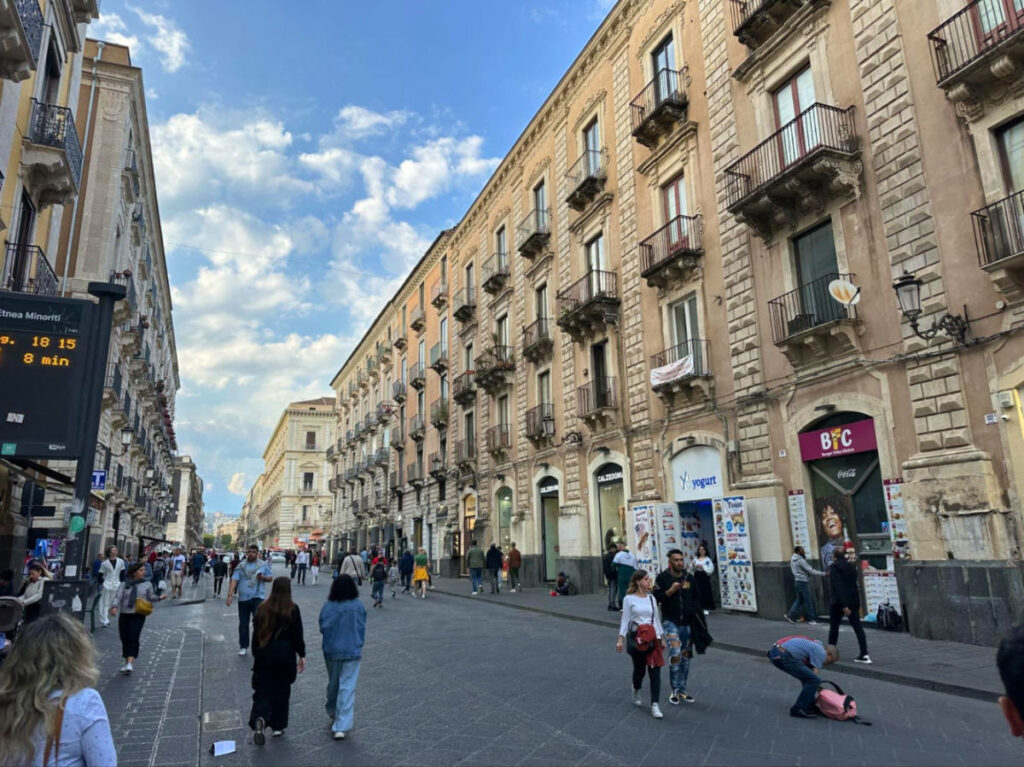 People strolling along a street filled with shops and eateries in Via Etnea