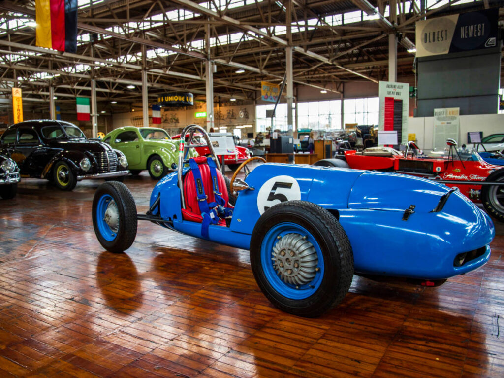 A vibrant blue vintage car displayed with other cars inside the Lane Motor Museum