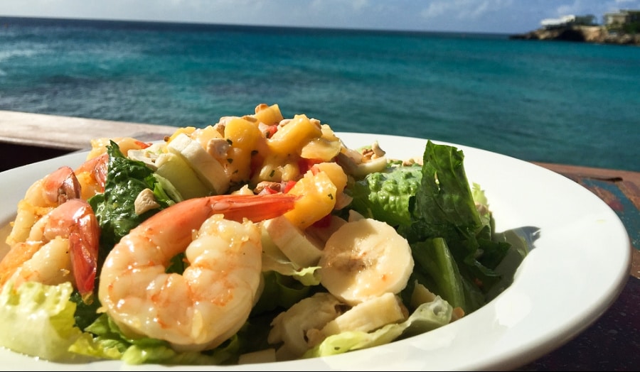A plate of banana, mango, and shrimp salad with a sea view