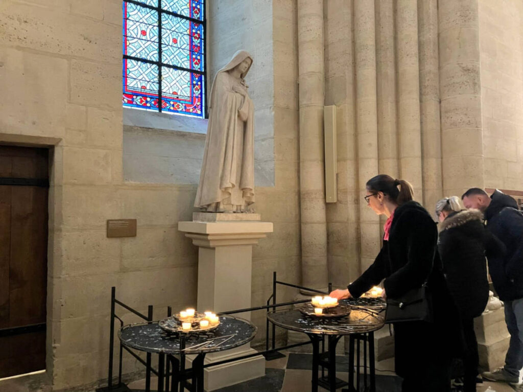 People lighting a candle in front of a statue of the Virgin Mary