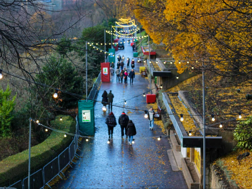 The people wandering around Princes Street Gardens with holiday lights around