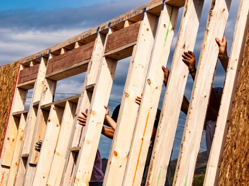 Hands of volunteers raising a wall for a Habitat for Humanity home