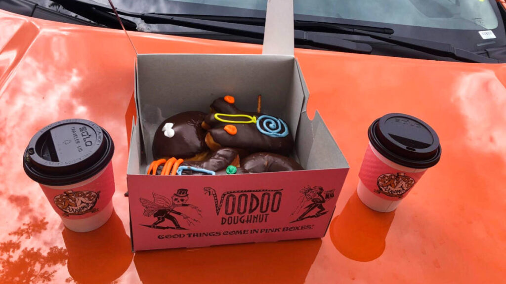 A box of Voodoo Doughnut and two cups of coffee on the hood of the car