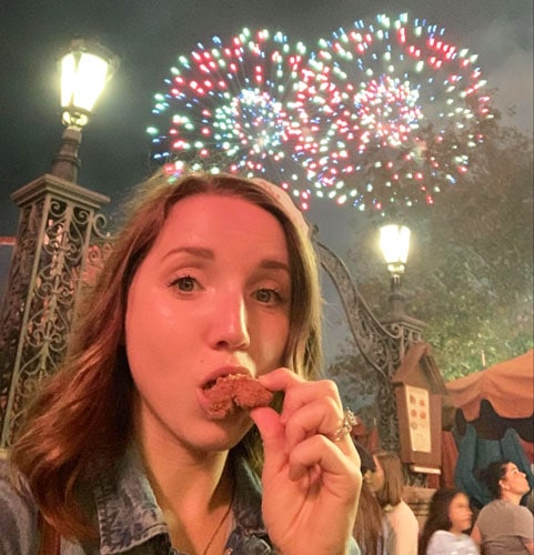 View of the author eating a chicken nugget and a colorful fireworks on her background