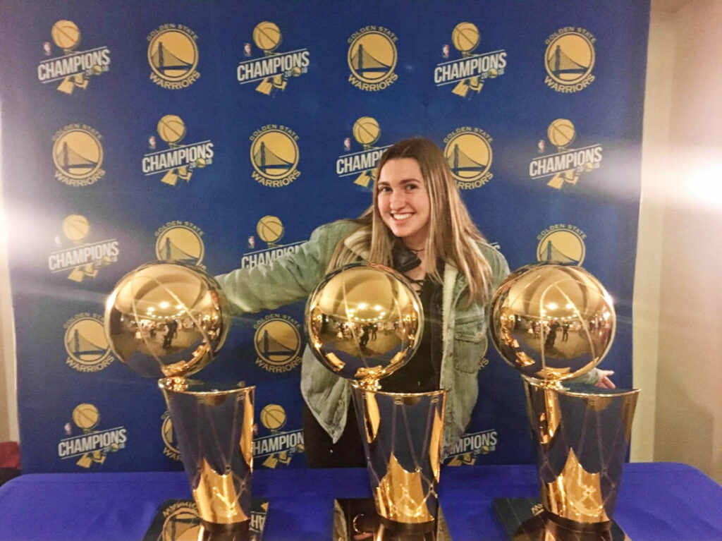 The author, Laura McFarland smiling for a photo with the Warriors’ NBA trophies