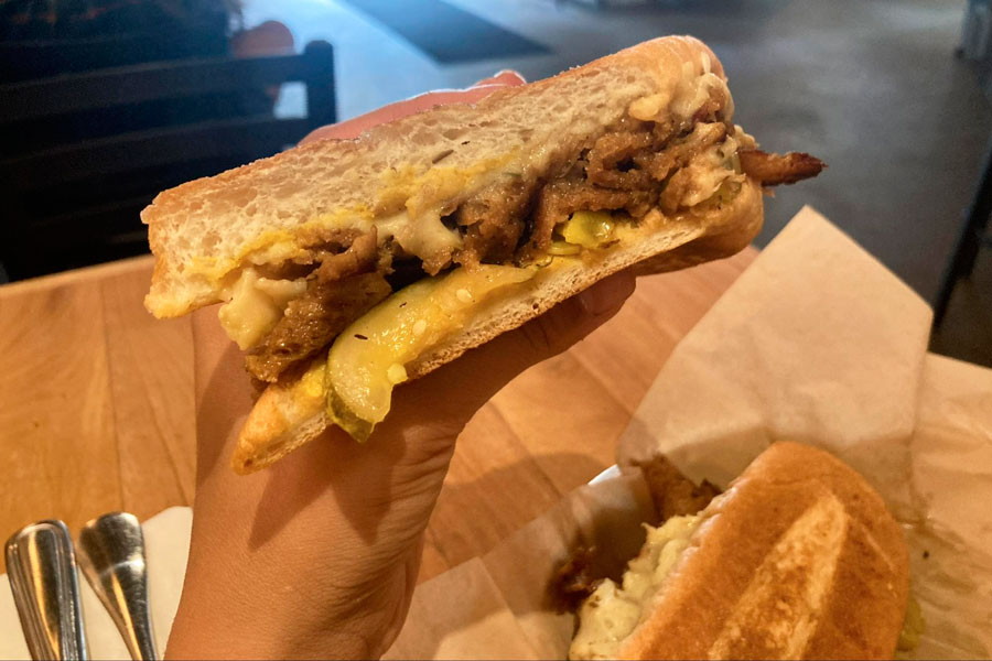 A hand holding a Cuban sandwich for vegan in Watercourse Foods