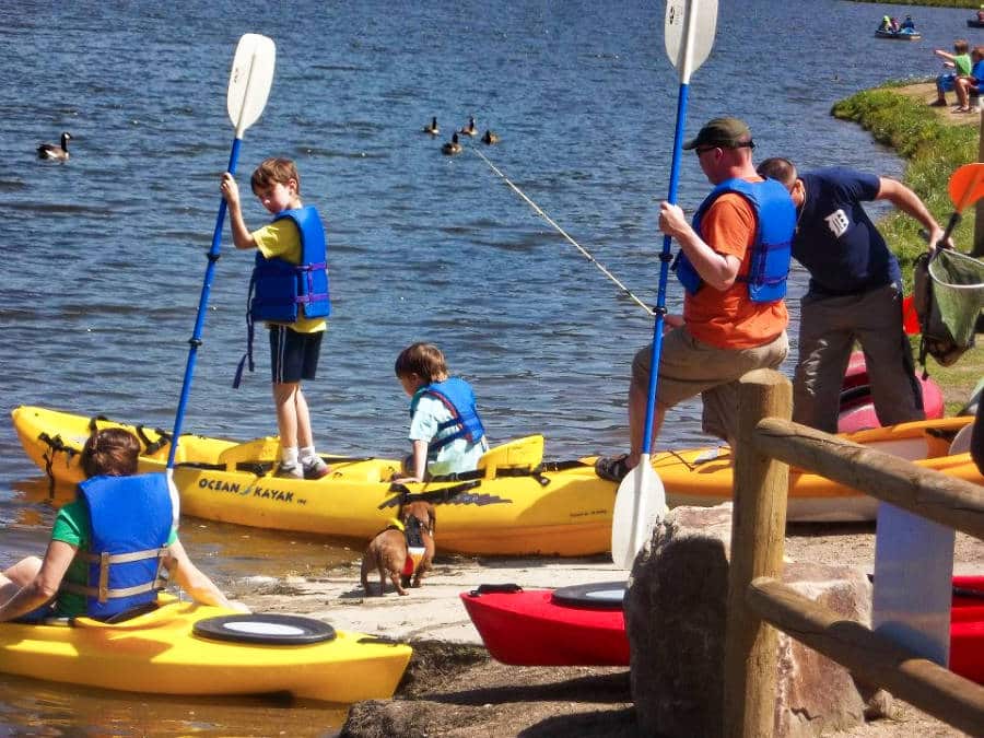 The man, children, and a dog wearing life jackets while getting ready to ride a kayak
