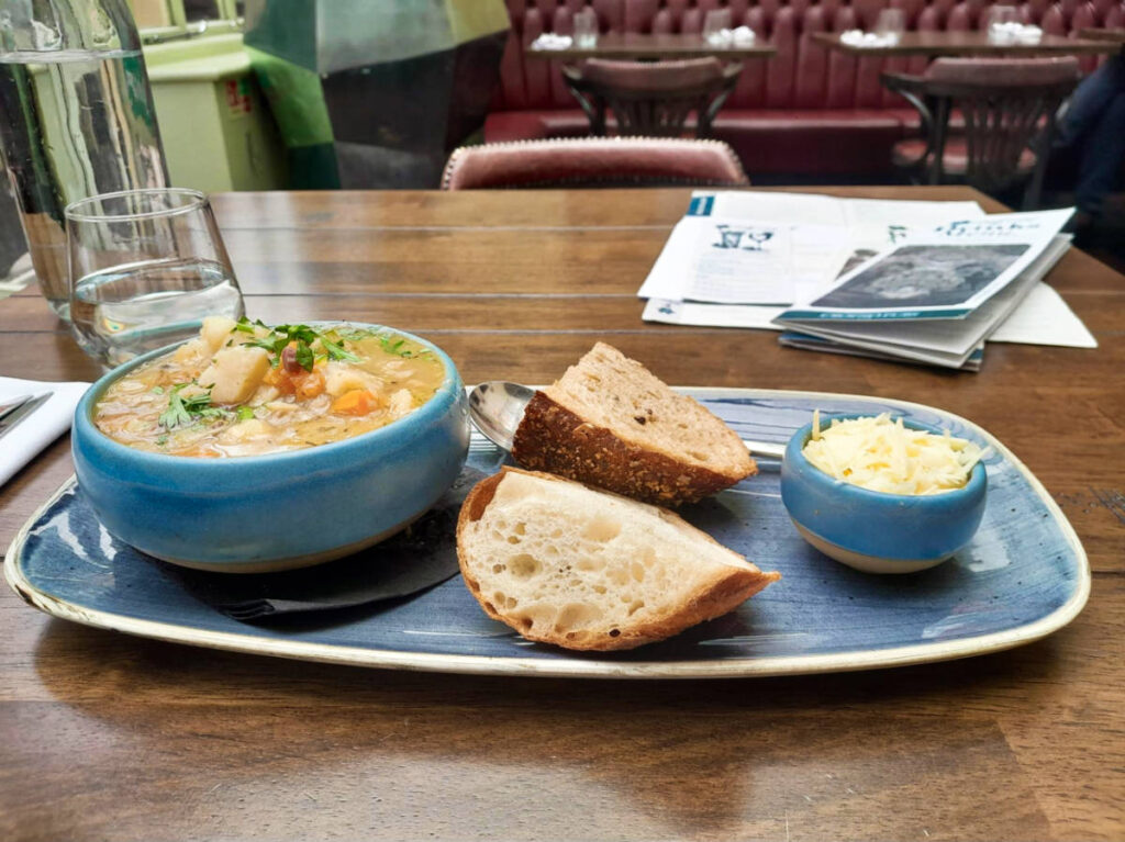 A bowl of traditional Welsh soup with bread and shredded cheese on the side