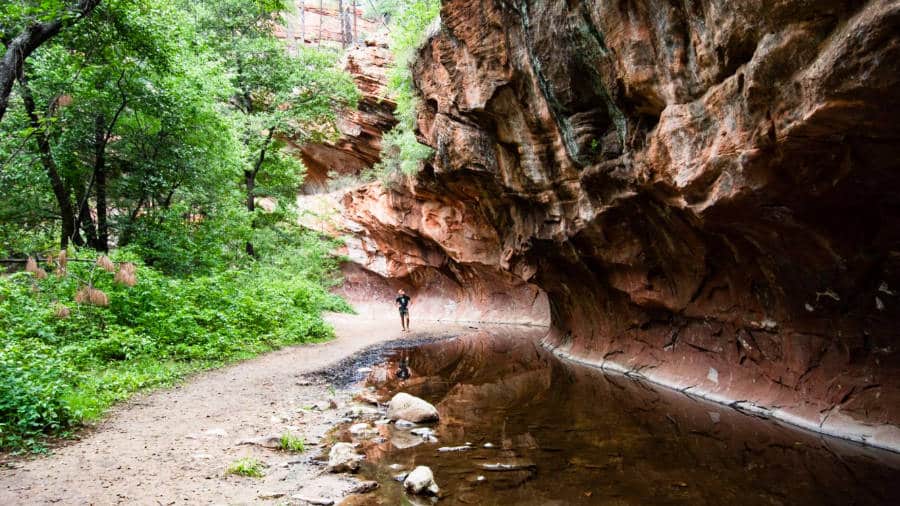 View from a distance of a man standing below the natural canyon and small river