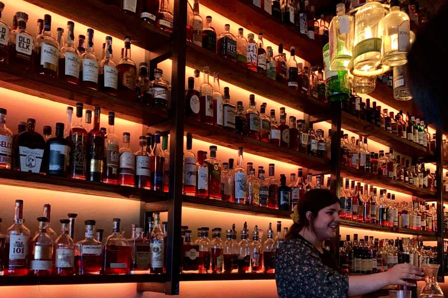 A bartender and a whiskey collection at Batch on her background