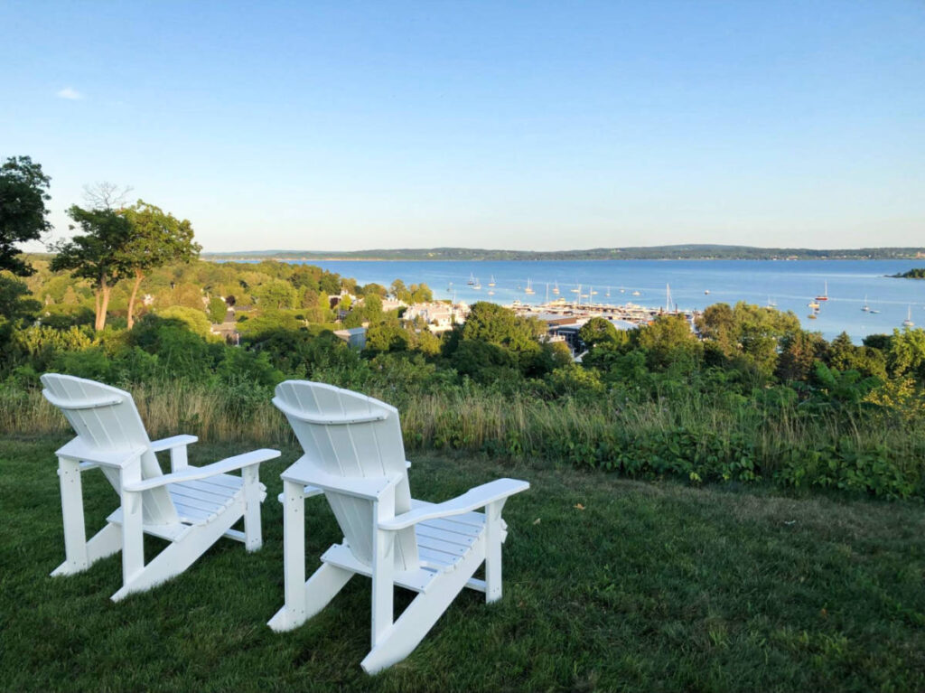 Two white chairs on the grass above Harbor Springs, overlooking the calm waters