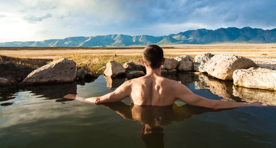 A man enjoying a dip in the hot spring with a stunning view of the mountains in Wild Willy's Hot Springs.