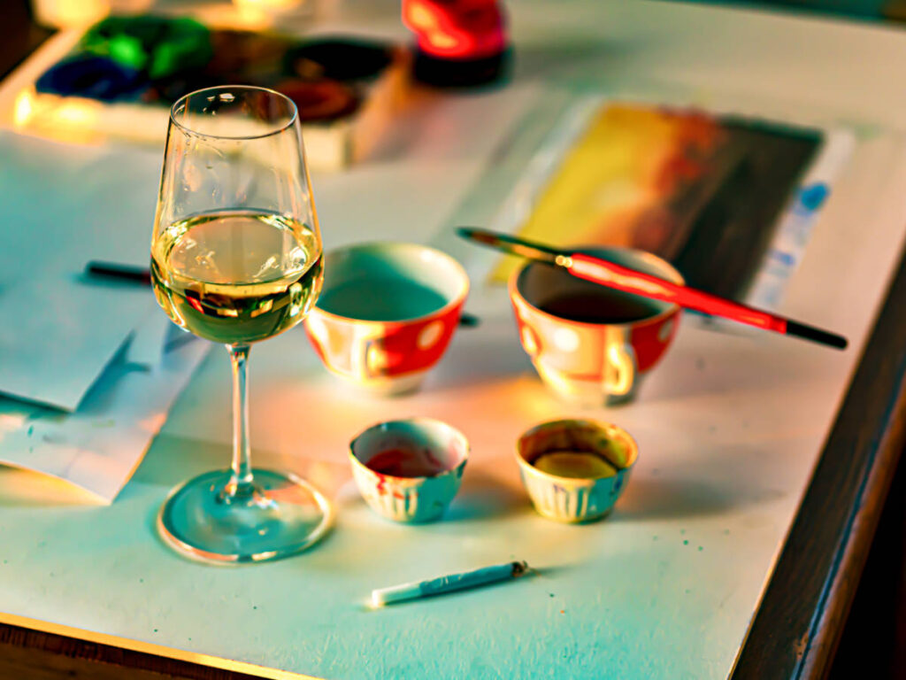 A glass of wine with paints, paintbrush and an artwork on the side