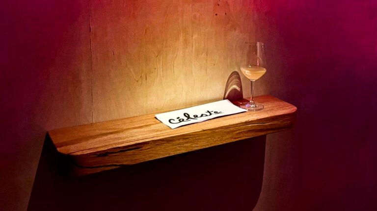 A wine glass and the menu of Céleste on a wooden shelf