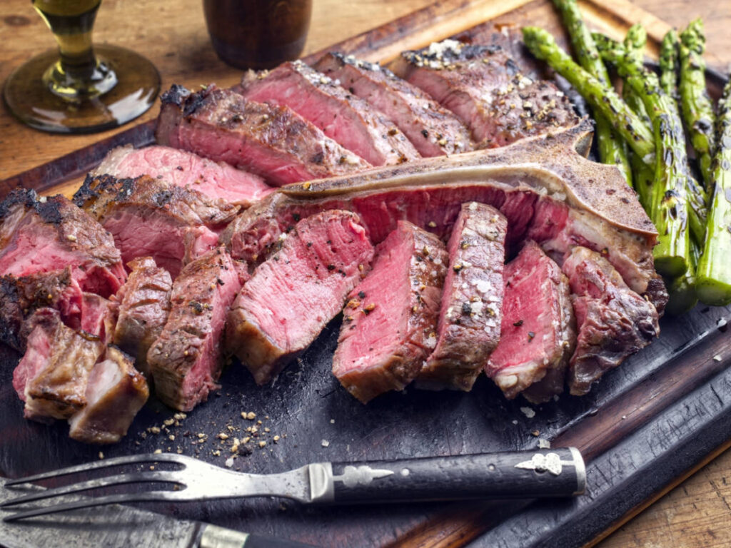 A medium rare steak and asparagus on a wooden board with fork and knife served in Witherspoon Grill