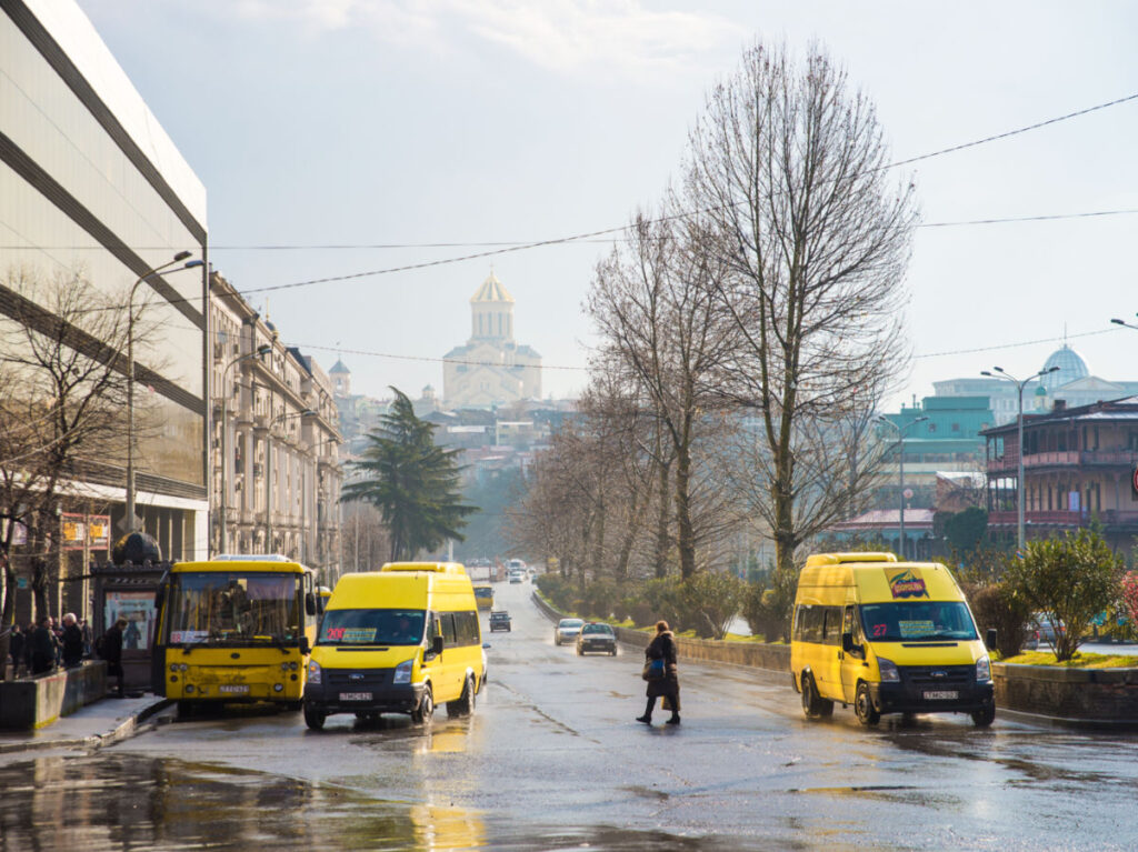 A woman crossing the road with public transportations in Tbilisi