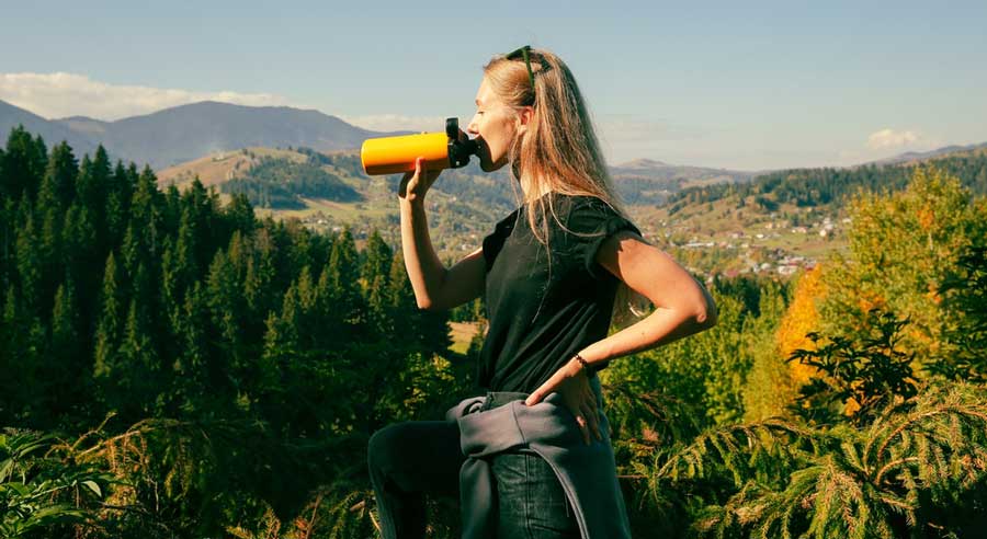 A woman drinking from her tumbler with a scenic view from her background