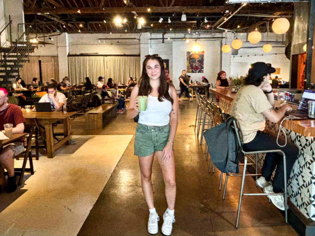 A woman holding a drink inside the Kahvi Coffee + Cafe