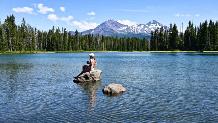 A woman sitting on a rock in the middle of Scott Lake with scenic mountain views
