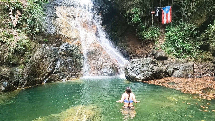 A woman enjoying the water while looking up at the waterfalls in Puerto Rico