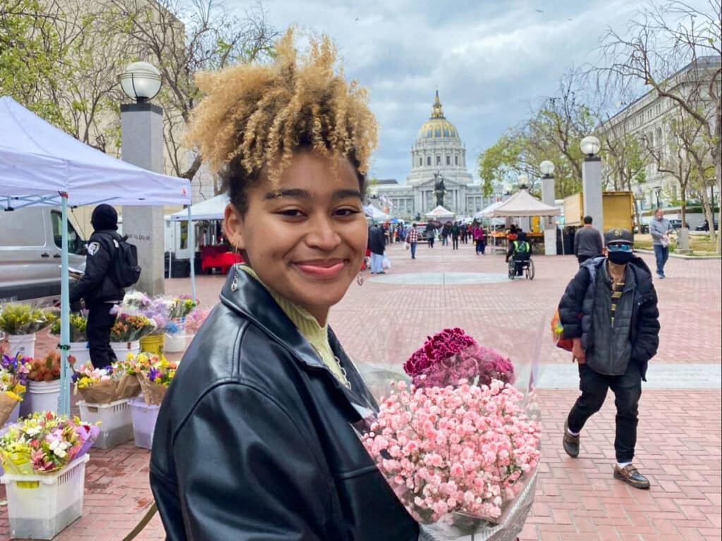 The author's roommate, Hunter, posing with a bouquet of pink flowers at the Farmers Market in front of the City Hall