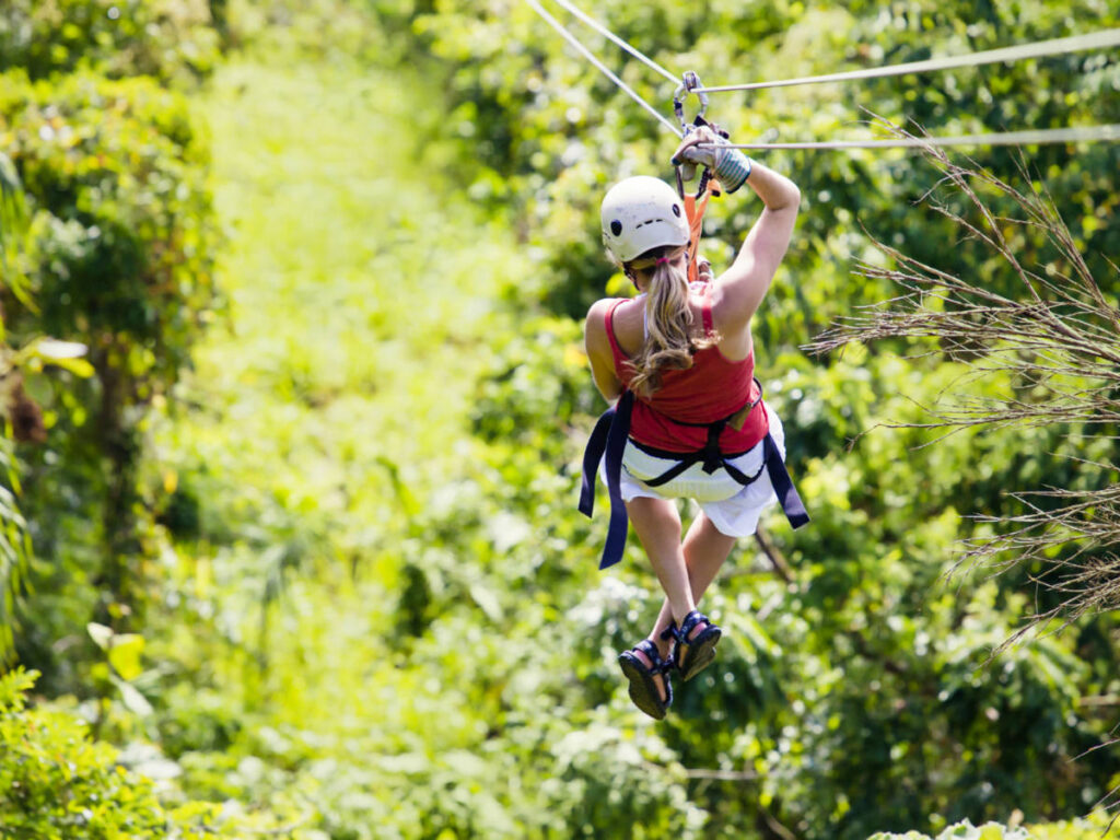 View of a woman's back ziplining over the lush rainforest