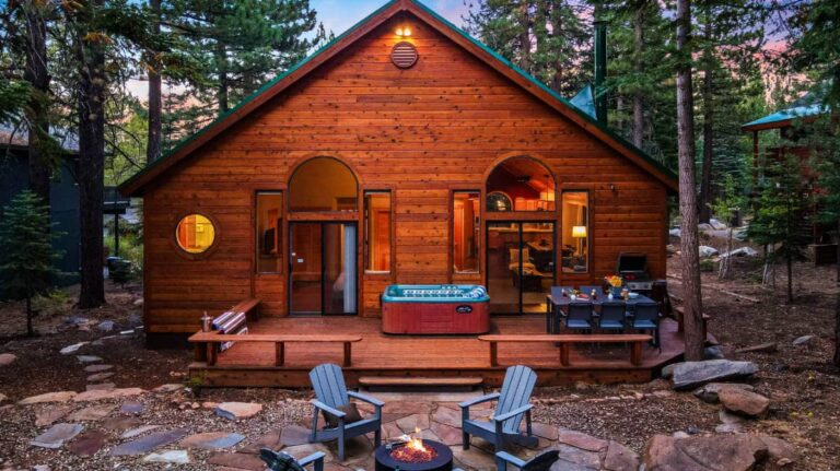 Façade of the wooden rental cabin with outdoor seating area in the middle of the forest