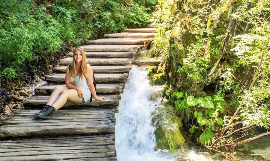 View of the author sitting on a wooden staircase in Plitvice Lakes National Park