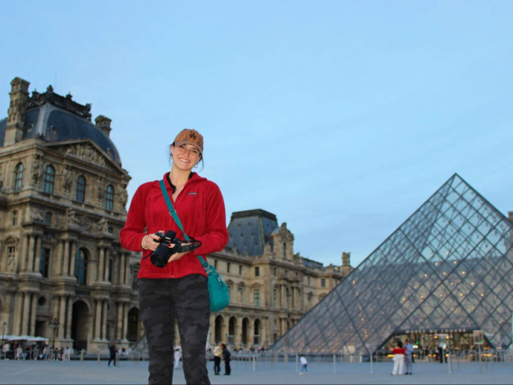 Writer Betty standing in front of the Louvre Museum while holding her camera