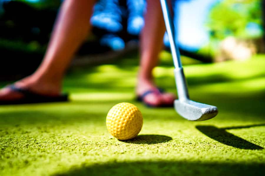A game of mini golf with a yellow ball and club at sunset