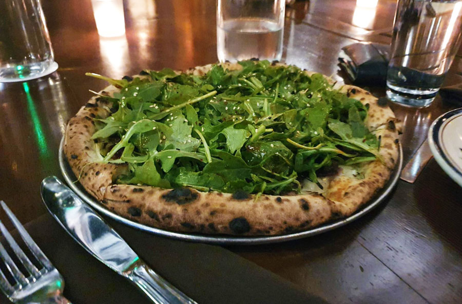A Korean BBQ pizza on a plate with fork and knife on the side