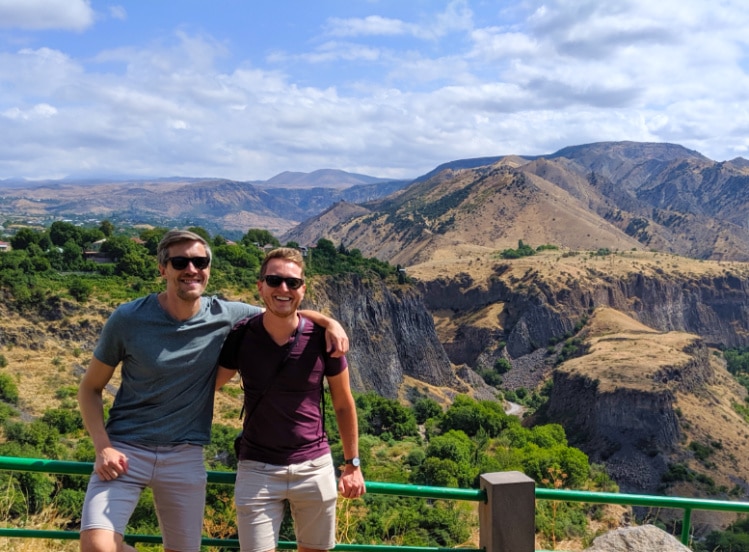 Author Nate with his travel buddy smiling brightly for a photo with the mountains of Armenia as their background