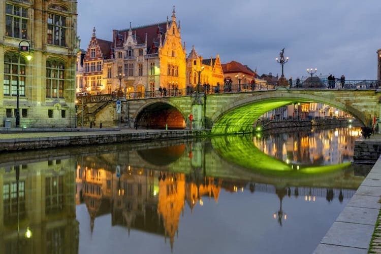 A river, a bridge, and old buildings all lit up at night in a city.