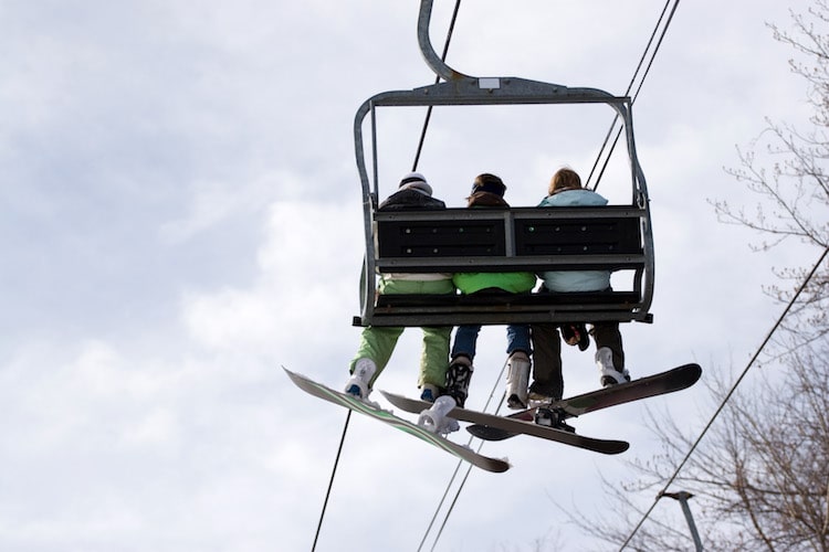 Three snowboarder friends ride the ski lift to the top of the hill