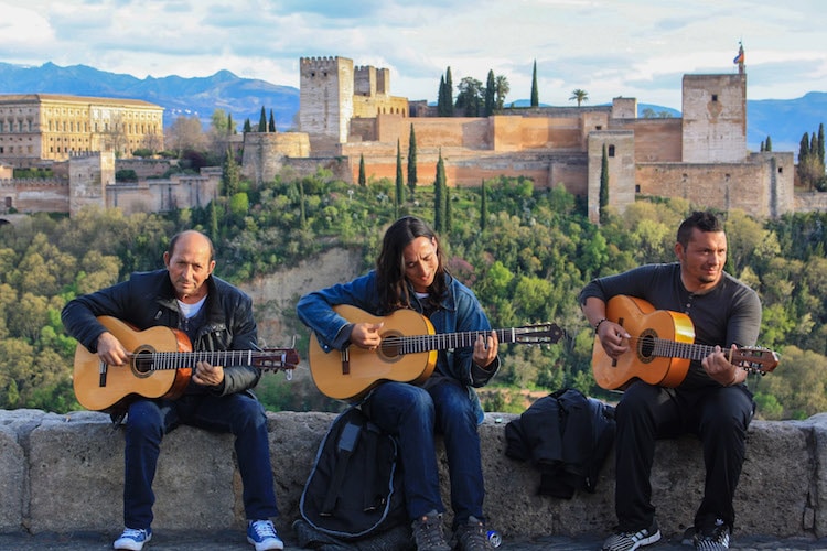 Three men play guitar in front of the Alhambra in Granada, Spain