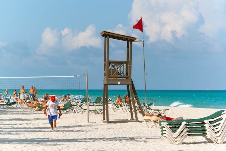 Calle 2 Beach with a lifeguard's station, lounge chairs, and people playing beach volleyball.