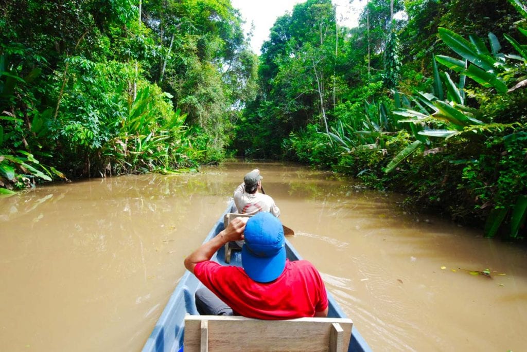 The men riding a boat on a river surrounded by greenery