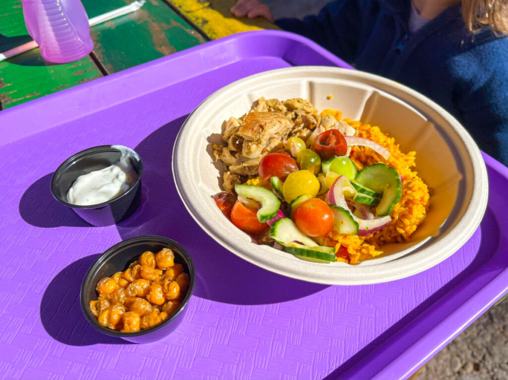 A purple tray with a chicken rice bowl and two small bowls filled with food and sauce at Harambe Market