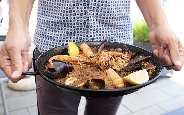 Closeup of a young man holding a typical spanish seafood paella in the paellera, the paella pan