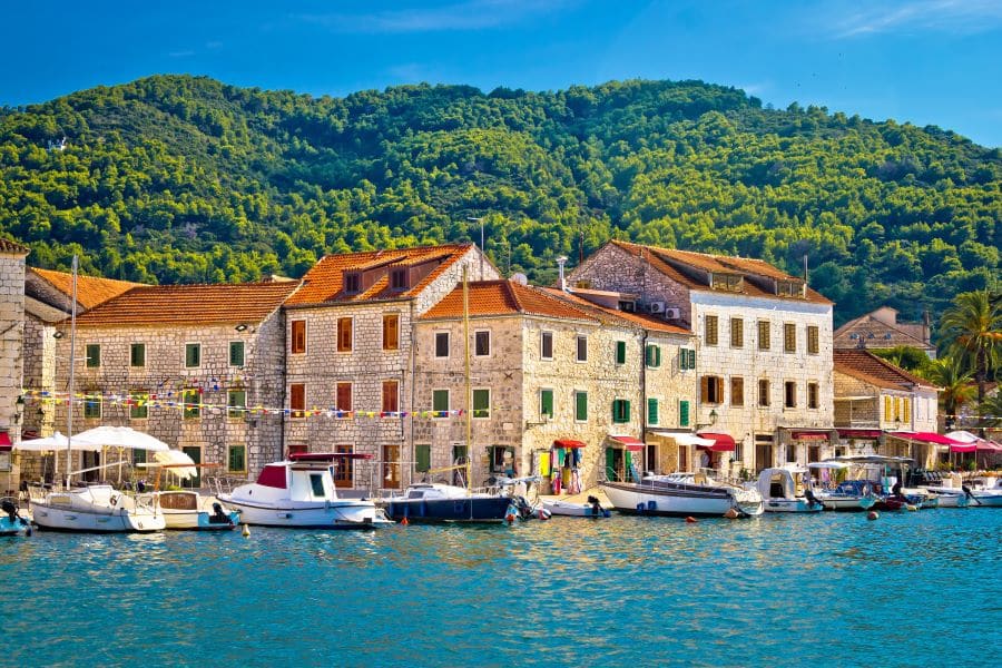 Old town of Stari Grad along the waterfront. Boats are docked in the harbor and flags fly in front of buildings.