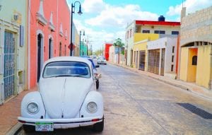 Colorful buildings line a street with old Volkswagen beetles parked outside